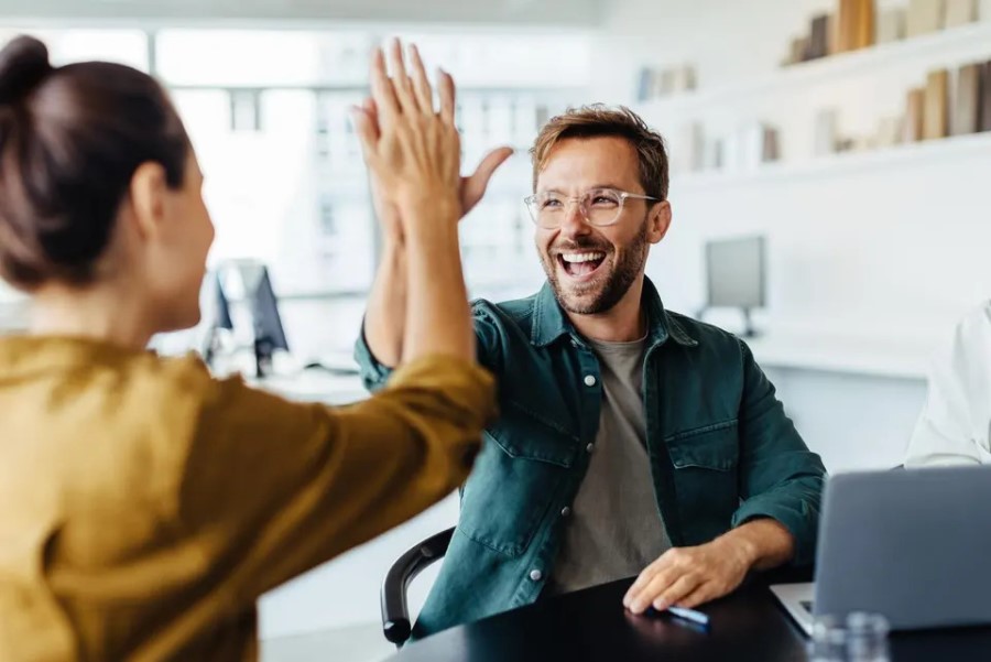 A man smiles as he receives a high-five from a coworker