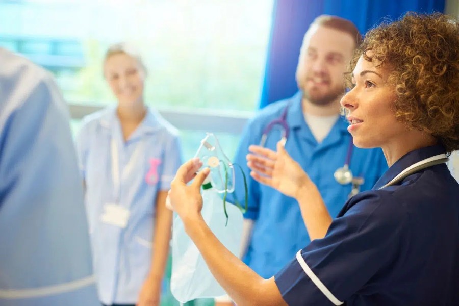 A doctor holds up an oxygen mask while teaching the medical staff around her